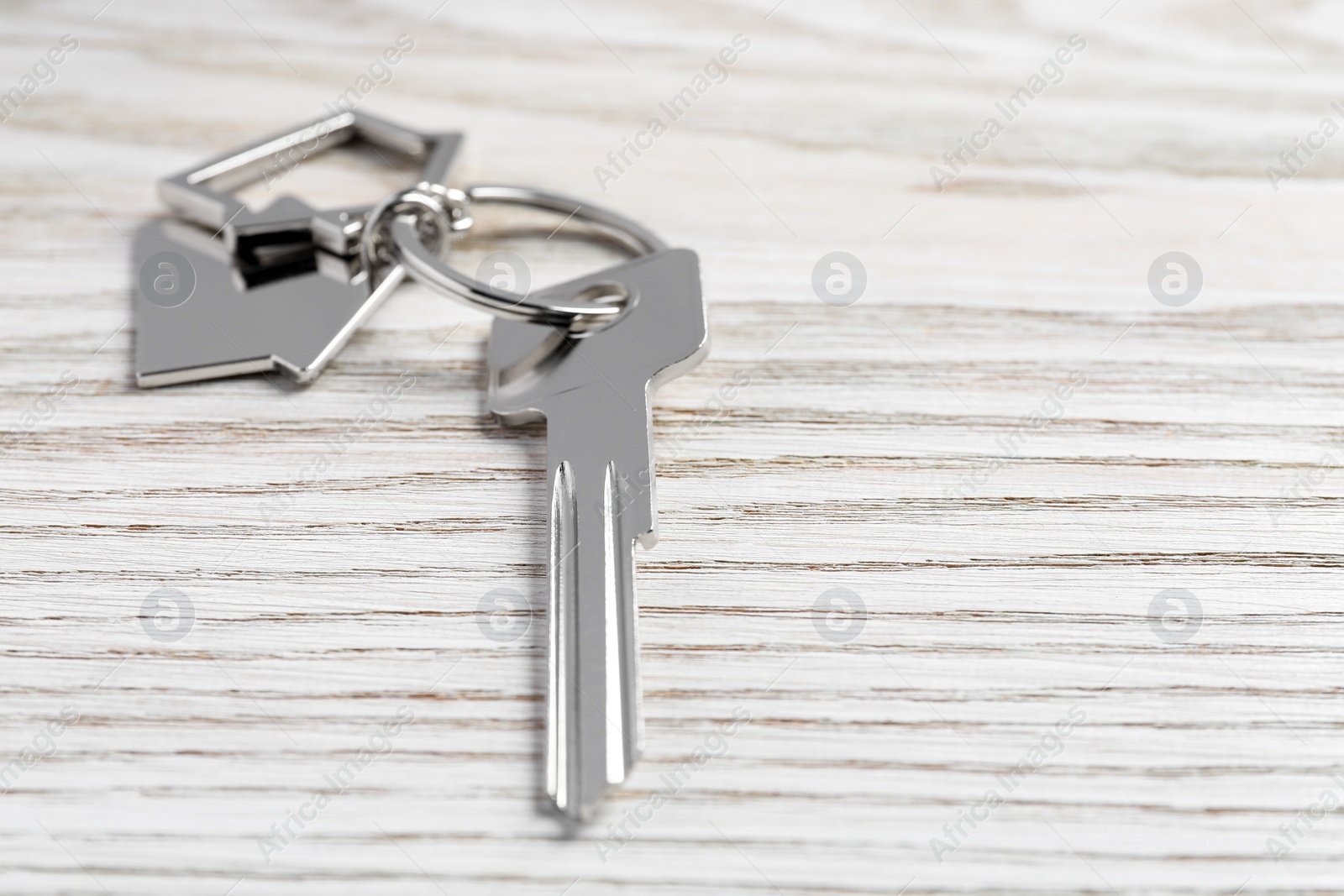 Photo of Key with keychain in shape of house on light wooden table, closeup. Space for text