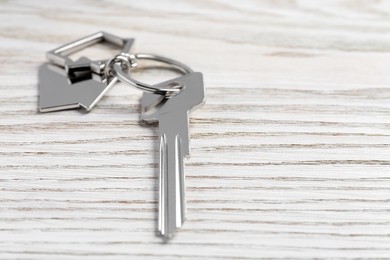 Photo of Key with keychain in shape of house on light wooden table, closeup. Space for text