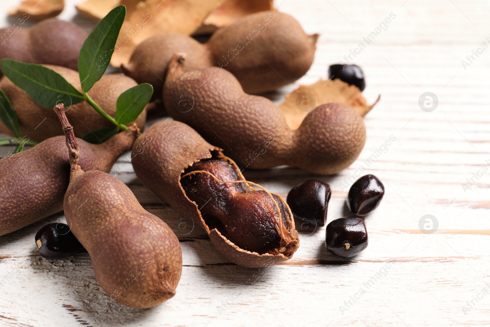 Photo of Delicious ripe tamarinds and leaves on white wooden table, closeup