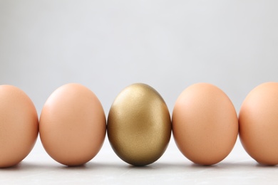 Photo of Golden egg among others on white table