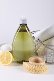 Bottle of cleaning product, brush, rags and lemon on light background