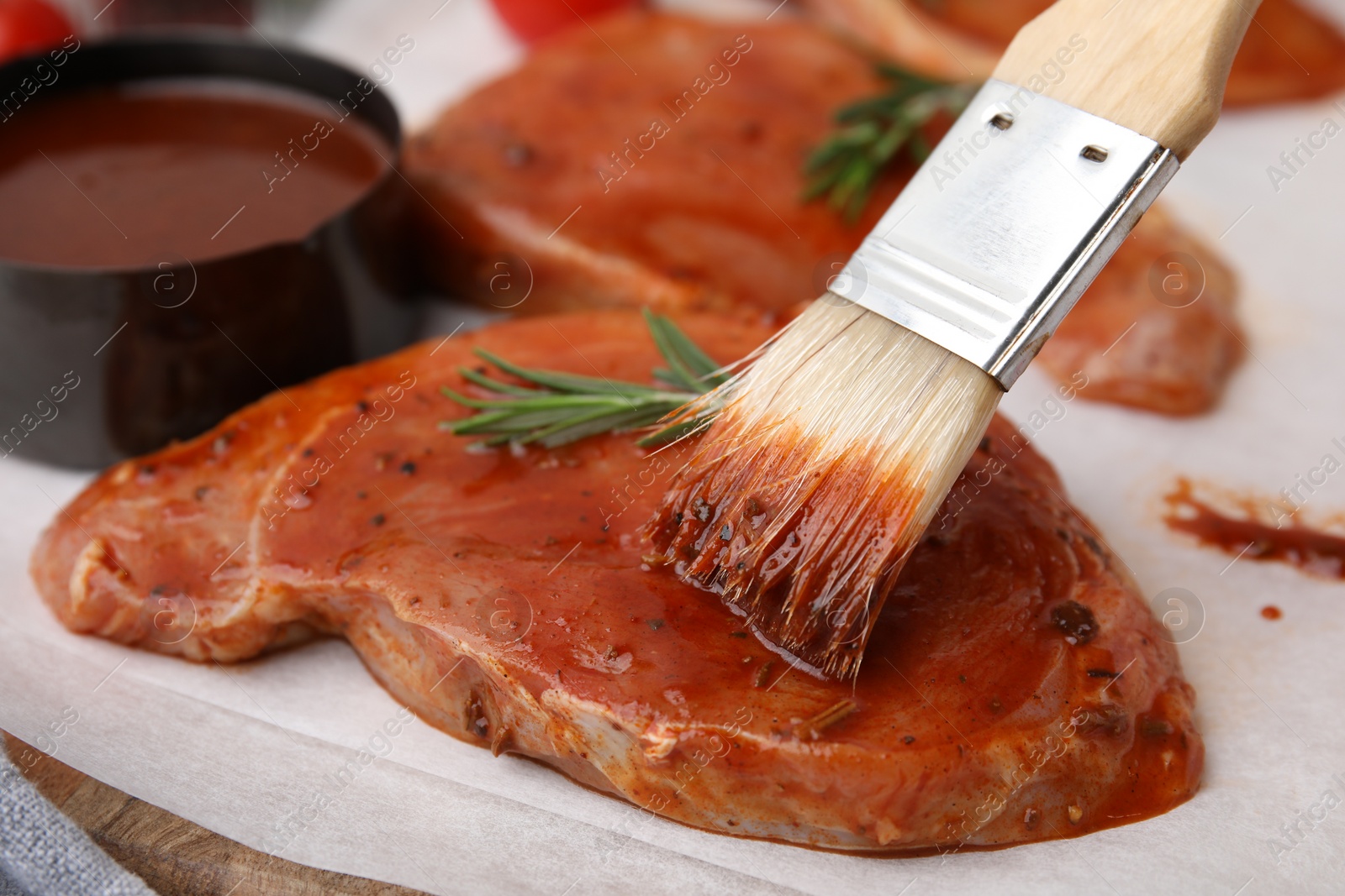 Photo of Spreading marinade onto raw meat with basting brush on table, closeup