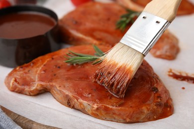 Spreading marinade onto raw meat with basting brush on table, closeup
