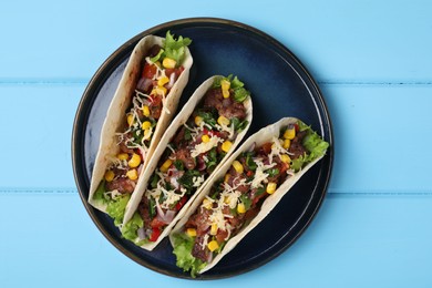 Photo of Delicious tacos with meat and vegetables on light blue table, top view