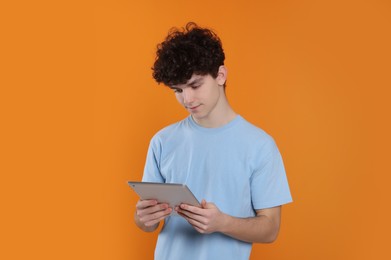 Teenage boy using tablet on orange background