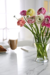 Photo of Beautiful fresh ranunculus flowers near cup of coffee and book on table in kitchen