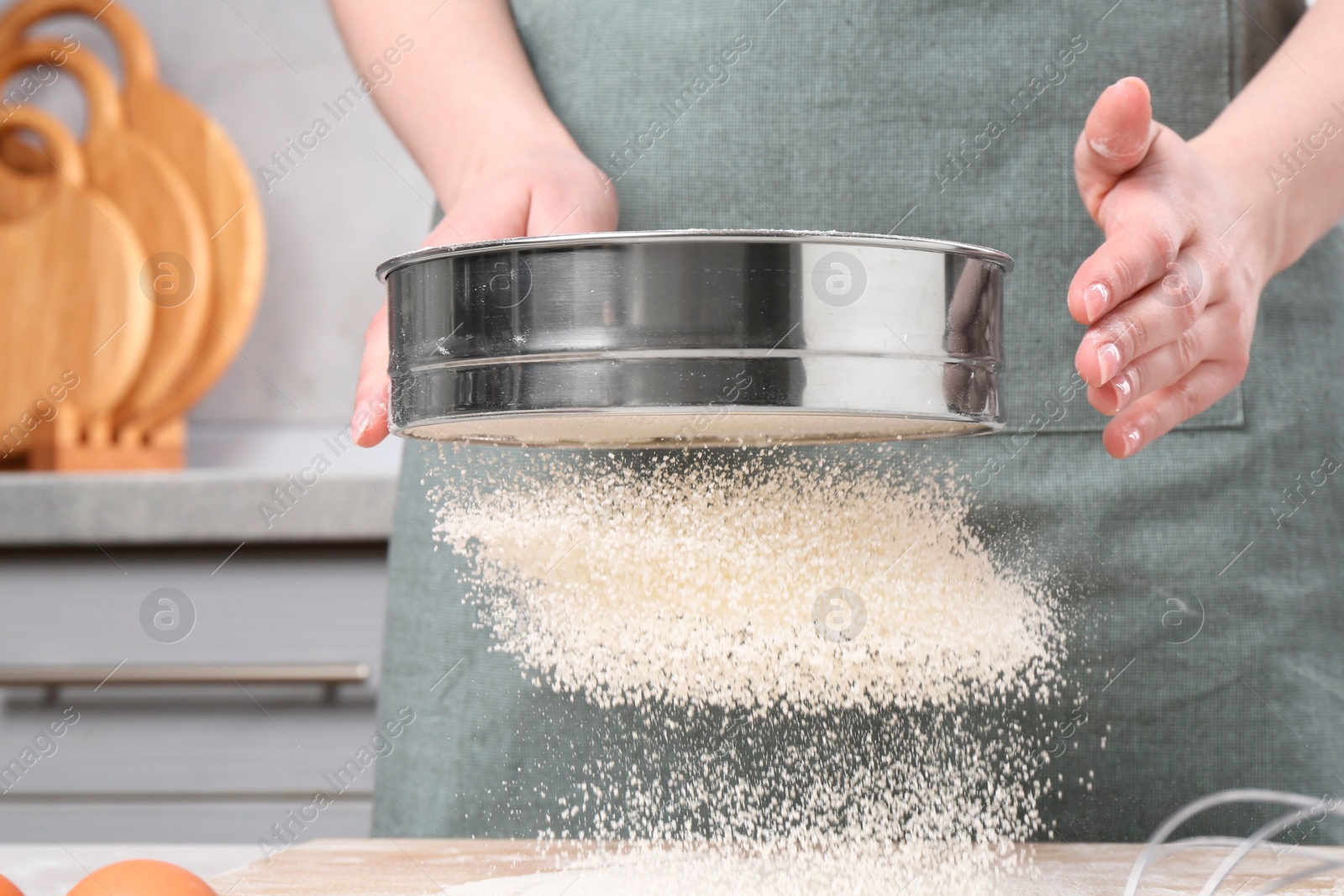 Photo of Woman sieving flour at table in kitchen, closeup