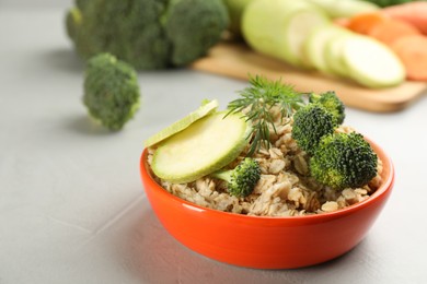 Photo of Feeding bowl with oatmeal porridge and vegetables on grey table, space for text. Natural pet food