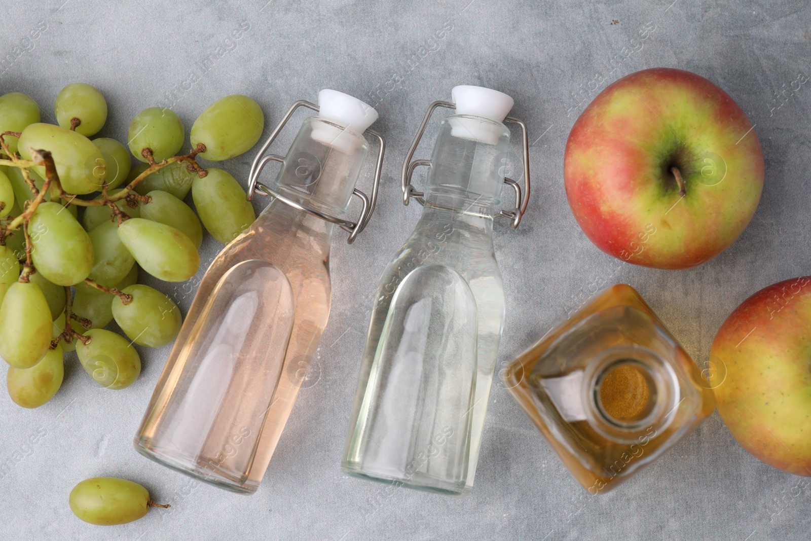 Photo of Different types of vinegar and fresh fruits on grey table, flat lay