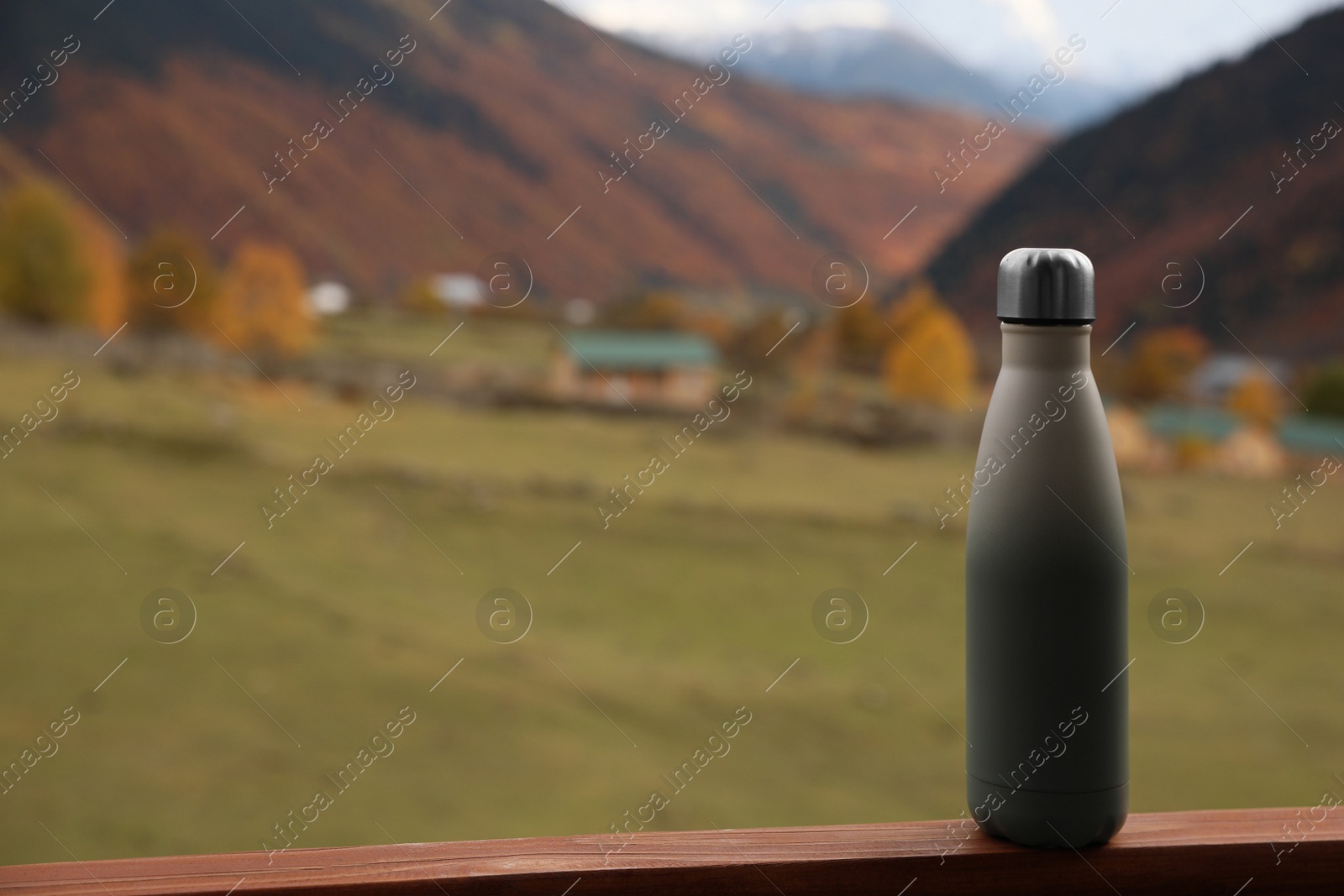 Photo of Thermo bottle on wooden surface in beautiful mountains. Space for text