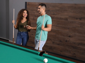 Young man and woman playing billiard indoors