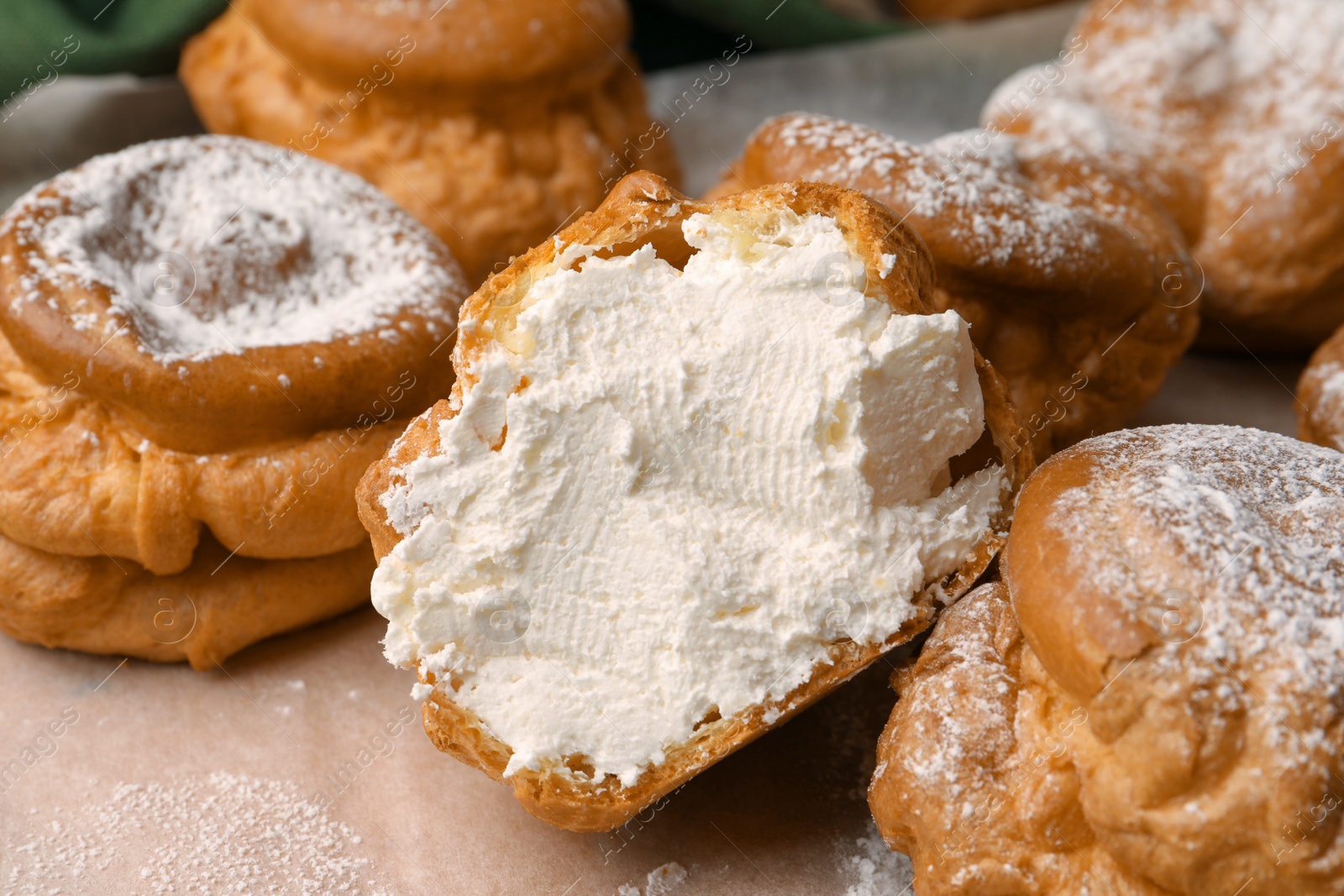 Photo of Delicious profiteroles filled with cream on parchment paper, closeup