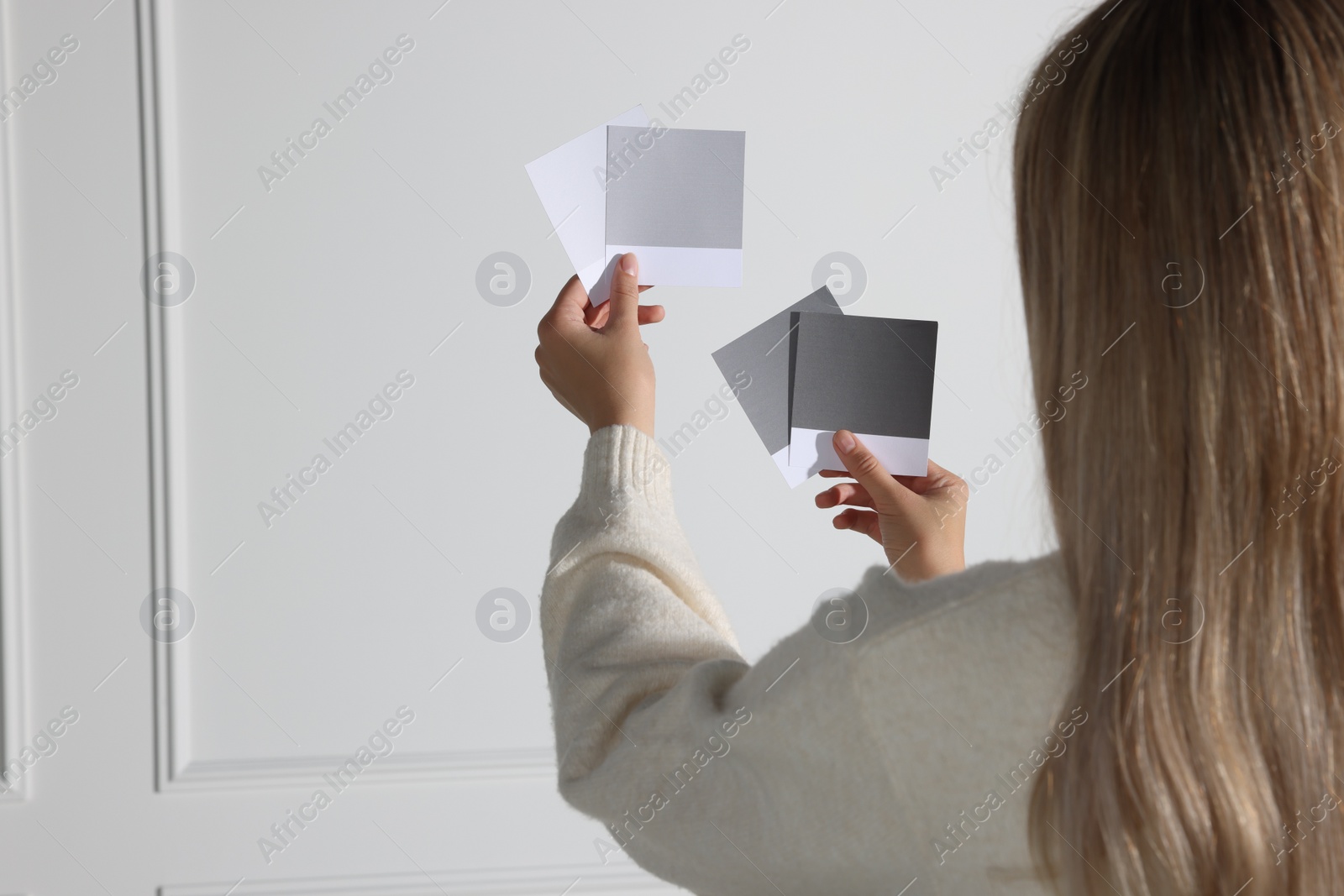 Photo of Woman choosing paint shade for wall indoors, focus on hands with color sample cards. Interior design