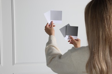 Photo of Woman choosing paint shade for wall indoors, focus on hands with color sample cards. Interior design