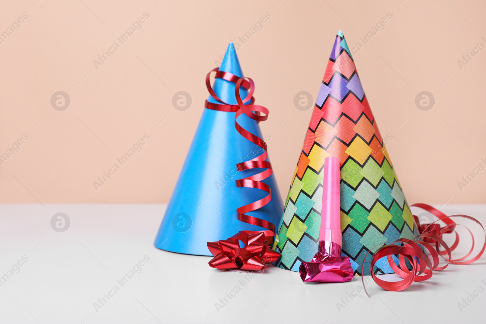 Photo of Colorful party hats, streamers and blower on white table, space for text. Birthday celebration