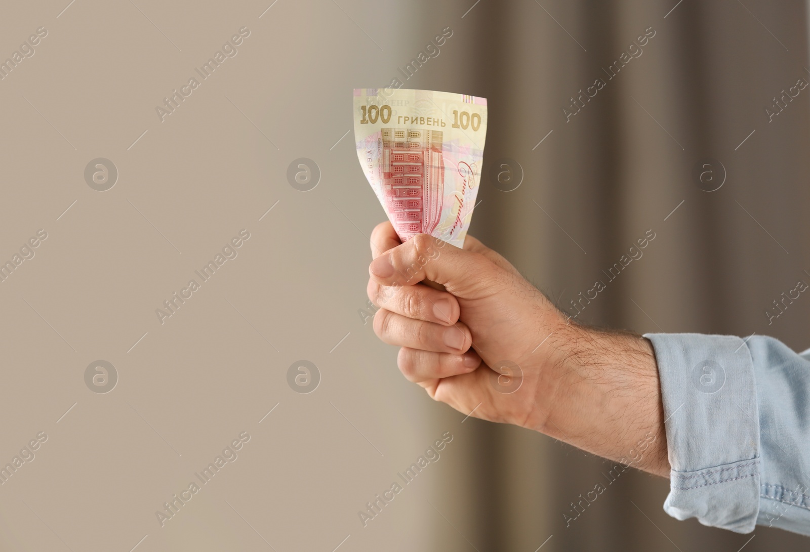 Photo of Man holding 100 Ukrainian Hryvnias banknote against blurred background, closeup with space for text. International relationships