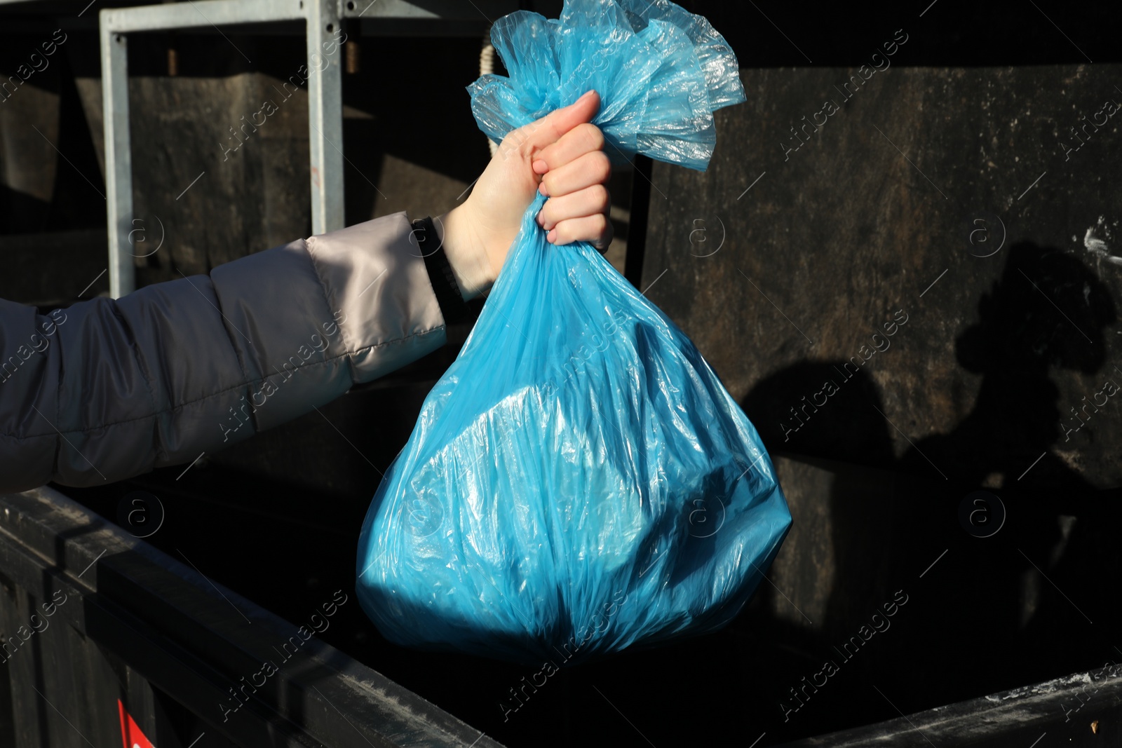 Photo of Woman throwing trash bag full of garbage in bin outdoors, closeup