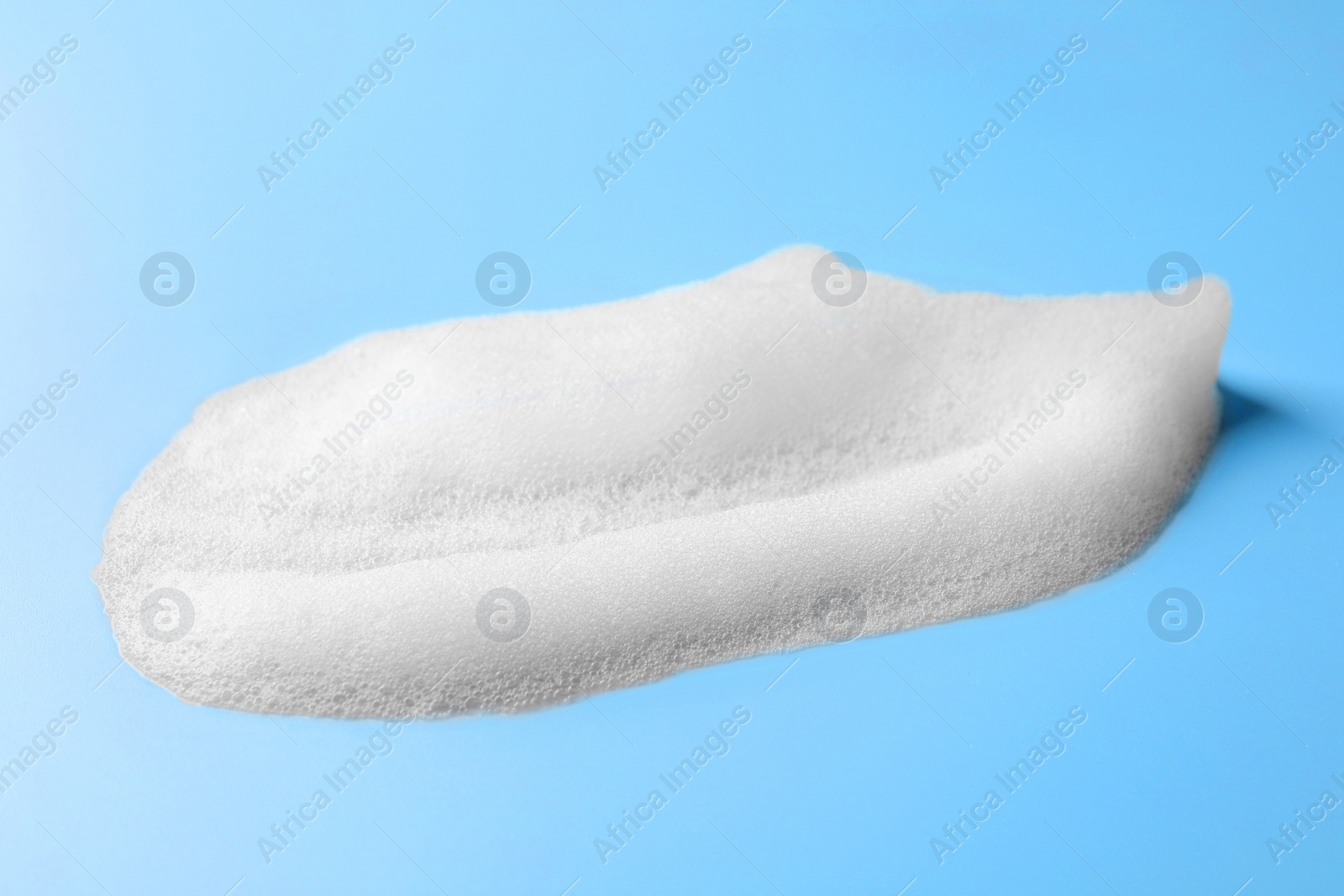 Photo of Drop of fluffy soap foam on light blue background