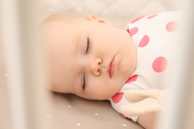 Photo of Cute baby girl sleeping in crib, closeup. Bedtime schedule