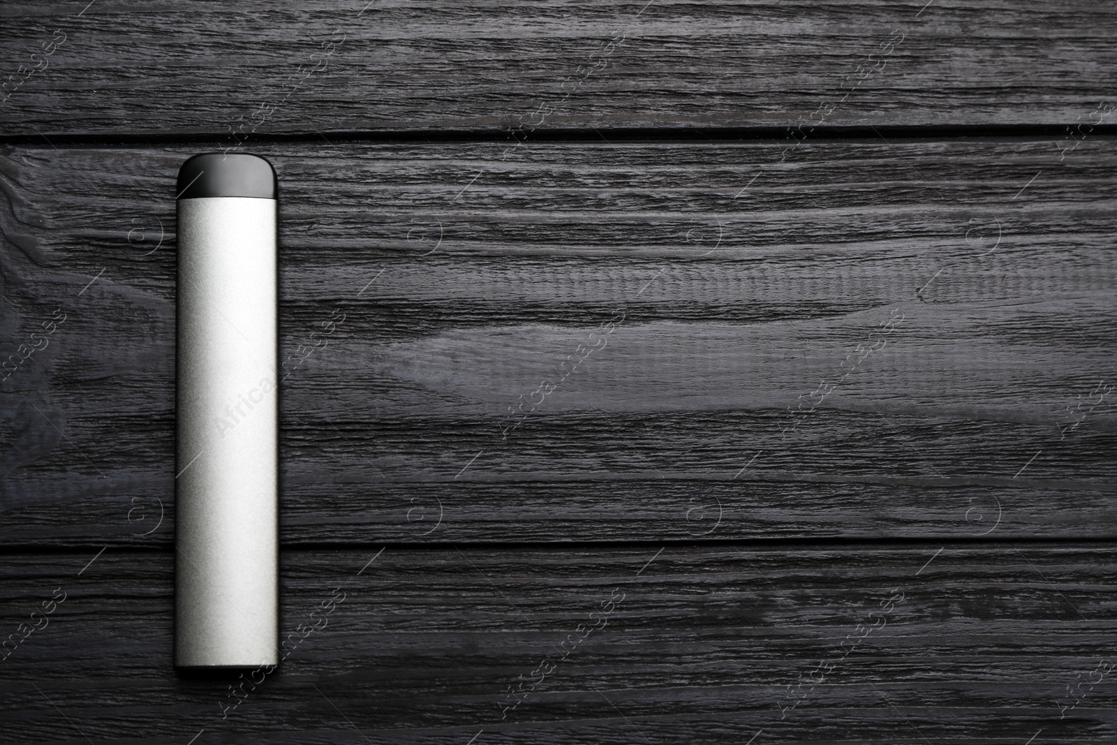 Photo of Disposable electronic cigarette on black wooden table, top view with space for text. Smoking alternative