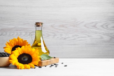 Sunflower cooking oil, seeds and yellow flowers on white wooden table, space for text