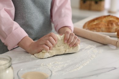 Making bread. Woman kneading dough at white table in kitchen, closeup