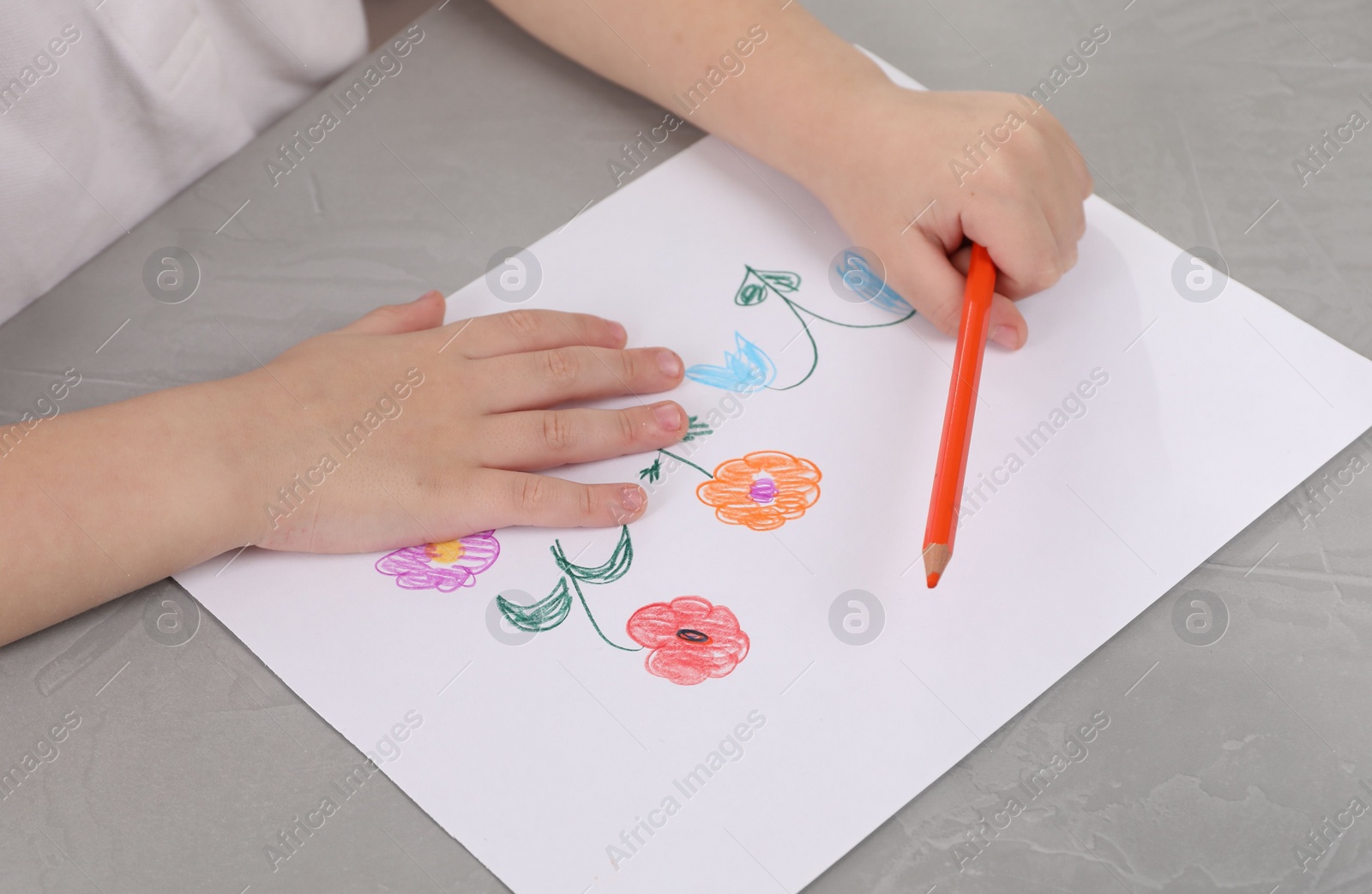 Photo of Little boy drawing flowers with pencil at grey textured table, closeup. Child`s art