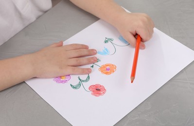 Little boy drawing flowers with pencil at grey textured table, closeup. Child`s art