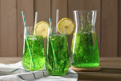 Photo of Jug and glasses of refreshing tarragon drink with lemon slices on wooden table