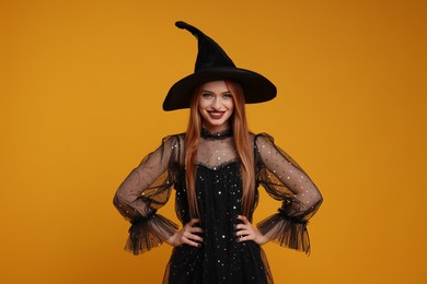 Photo of Happy young woman in scary witch costume on orange background. Halloween celebration