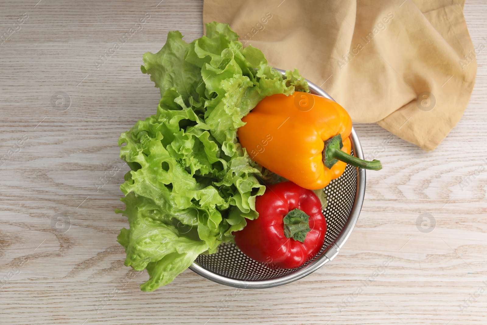 Photo of Colander with fresh lettuce and bell peppers on wooden table, top view