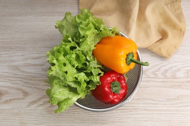 Photo of Colander with fresh lettuce and bell peppers on wooden table, top view