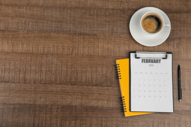 Photo of Flat lay composition with calendar and cup of coffee on wooden table. Space for text