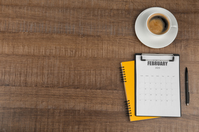 Flat lay composition with calendar and cup of coffee on wooden table. Space for text