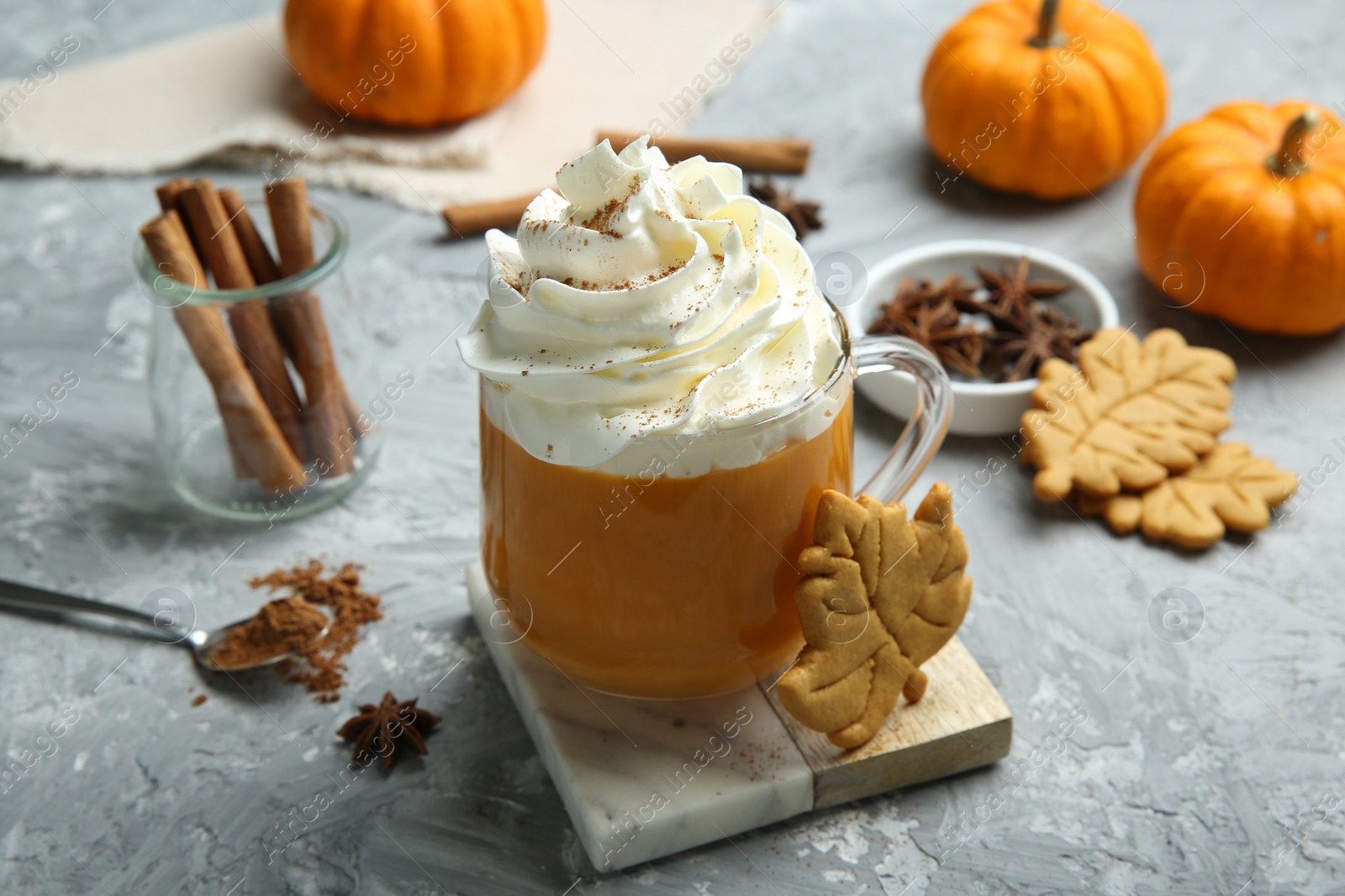 Photo of Cup of pumpkin spice latte with whipped cream, cookies and ingredients on light grey table