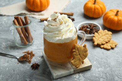 Cup of pumpkin spice latte with whipped cream, cookies and ingredients on light grey table