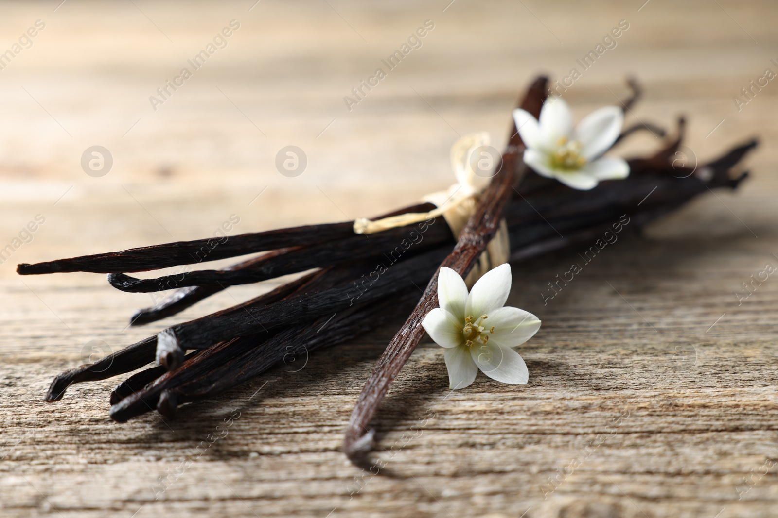 Photo of Bunch of vanilla pods and flowers on wooden table, closeup