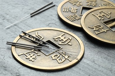 Photo of Acupuncture needles and Chinese coins on grey textured table, closeup