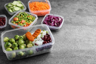 Set of plastic containers with fresh food on grey   table, space for text