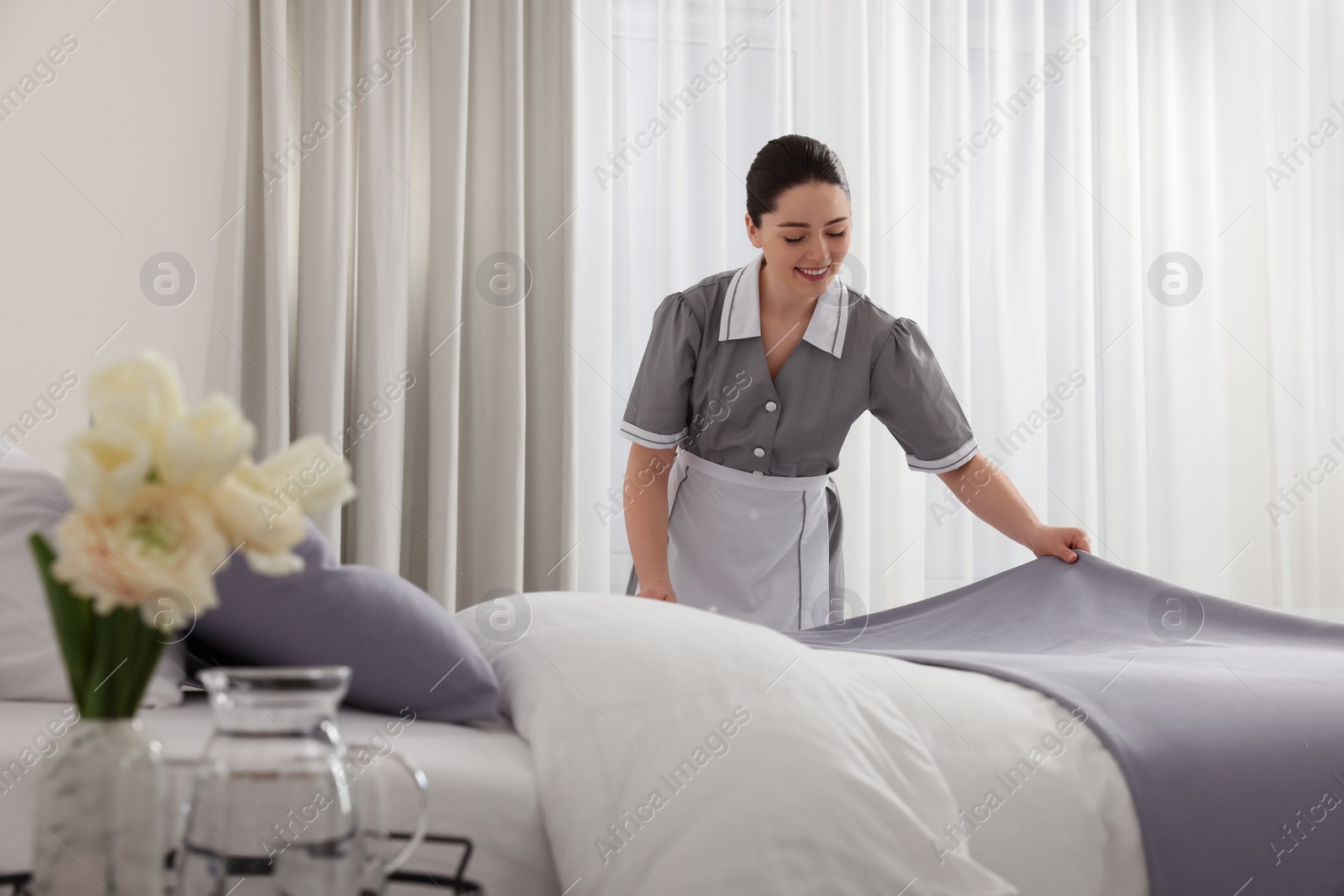 Photo of Young chambermaid making bed in hotel room