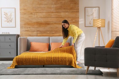 Photo of Young woman making bed in room. Modern interior with sleeper sofa
