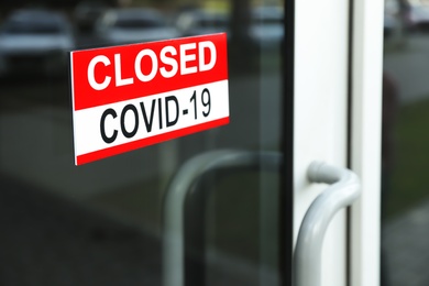 Photo of Red sign with words "Closed Covid-19" hanging on glass door