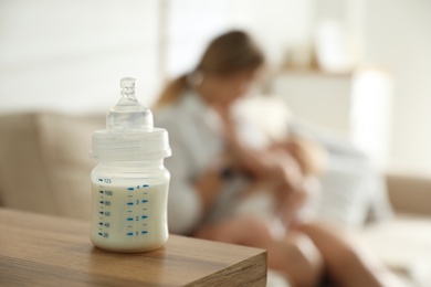 Photo of Mother breastfeeding her little baby at home, focus on bottle with milk. Healthy growth