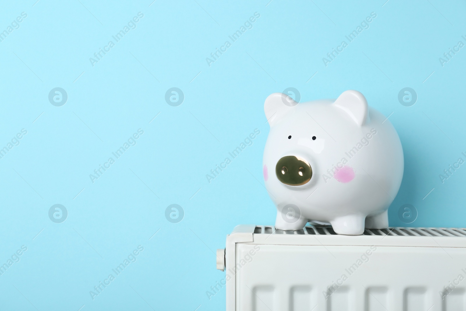 Photo of Piggy bank on heating radiator against light blue background, space for text