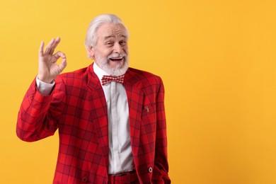 Photo of Portrait of grandpa with stylish red suit and bowtie showing ok gesture on yellow background, space for text
