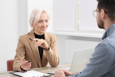 Photo of Happy woman having conversation with man at wooden table in office. Manager conducting job interview with applicant