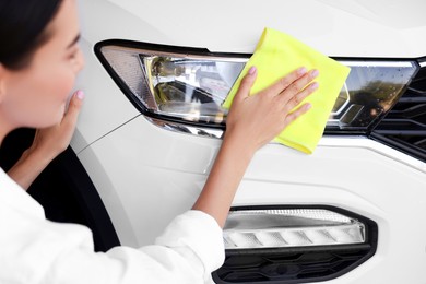 Photo of Woman cleaning car headlight with rag, closeup view