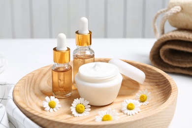 Photo of Composition with chamomile flowers and cosmetic products on wooden plate, closeup