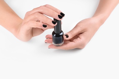 Woman with black manicure holding nail polish bottle on white background, closeup