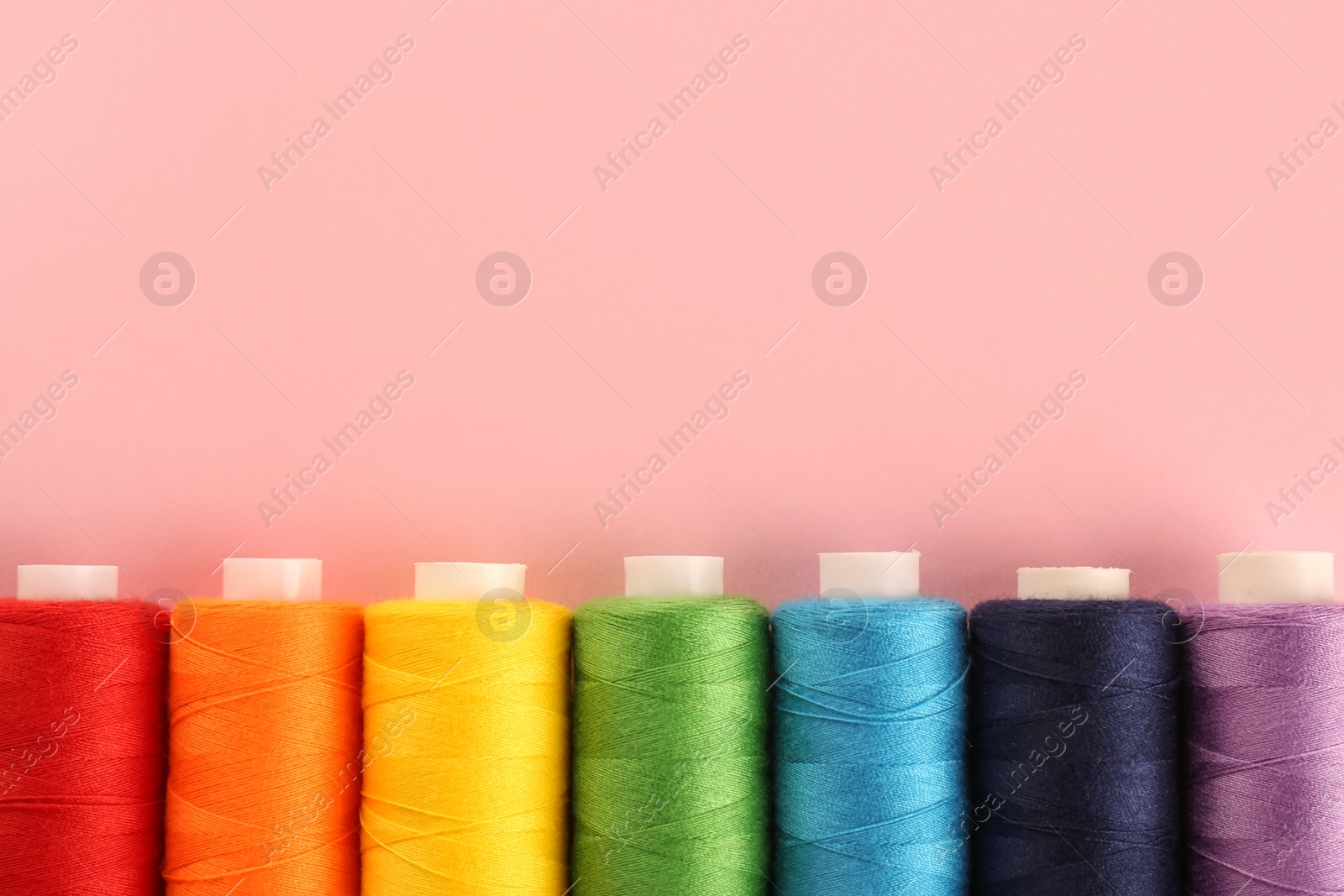 Photo of Different colorful sewing threads on pink background, flat lay. Space for text